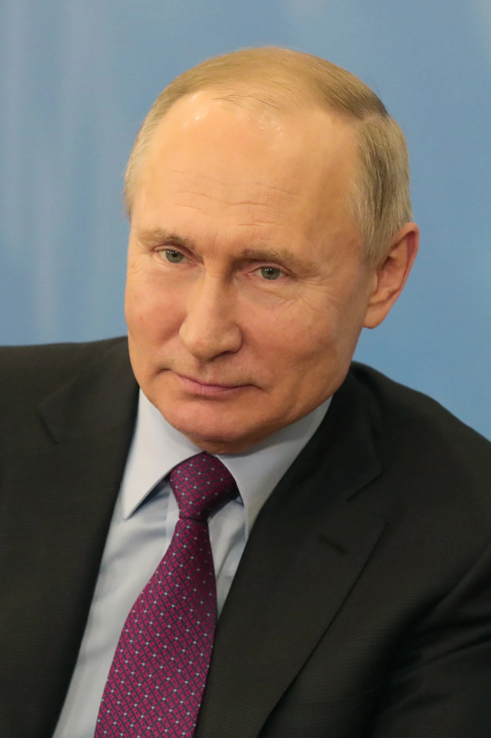 Портрет Володимира Путіна в костюмі з червоною краваткою на синьому тлі
